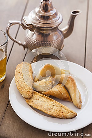A selection of Moroccan pastries on a plate. To the left a glass of mint tea and in the back a traditional tea pot Stock Photo