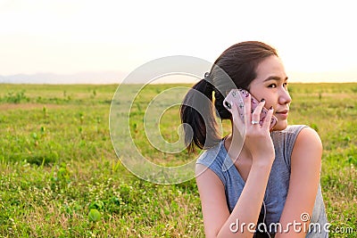 Selective focus of Asian women taking on mobile phone with green grass and sunset nature background Stock Photo