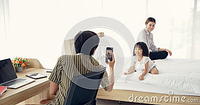 Selective focus of Asian young Fatherâ€™s mobile phone to take a cute photo of his little daughter at bedroom Stock Photo