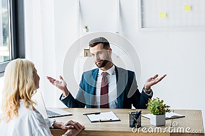 Focus of bearded recruiter showing shrug gesturing and looking at blonde employee Stock Photo