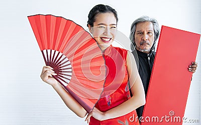 Selective focus beautiful happy Asian rich woman wearing red qipao or dress, smiling, holding folding fan with blur male bodyguard Stock Photo