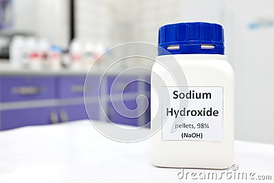 Selective focus of a bottle of pure sodium hydroxide or NaOH chemical compound beside a petri dish with white solid pellets. Stock Photo