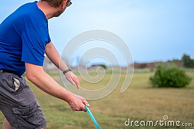 Selective focus on a Caucasian adult preparing to sidearm throw a disc golf towards the pin. Stock Photo