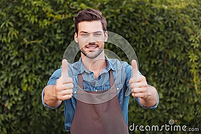 Cheerful gardener in apron showing thumbs up and looking at camera Stock Photo