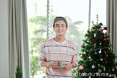 selective focus of cheerful man holding cup near christmas tree in living room Stock Photo