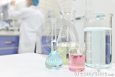 Selective focus of colored laboratory chemicals with blurred male scientist working on the background. Stock Photo