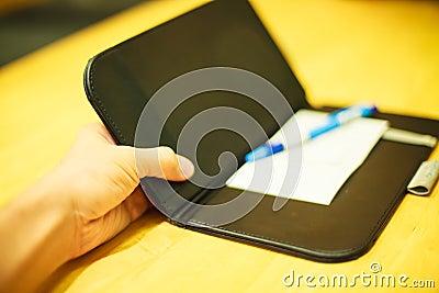 Selective focus customer hand receive bill payment receipt in black leather folder holder tray on yellow wooden table background Stock Photo