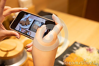 Selective focus at device screen. Women hand using smartphone to take photo of Japanese food for send or share with her friend or Stock Photo