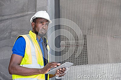 Selective focus at face of Black African foreman at building construction site, wearing protective hat and safety equipment while Stock Photo