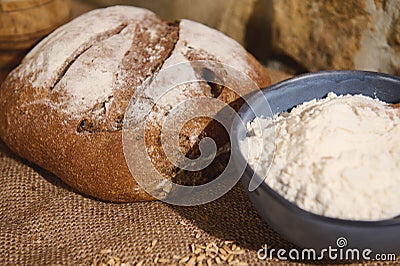 Selective focus on fresh baked homemade traditional sourdough bread, and a blue ceramic bowl with white flour on burlap Stock Photo