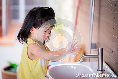 Selective focus. Girl wash their hands in the white sink. Child rub their hands with white soap bubble. Stock Photo