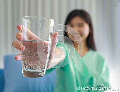 Selective focus on glass. Young inpatient woman who is getting well from her ailment smiling on to a camera and holding a glass Stock Photo