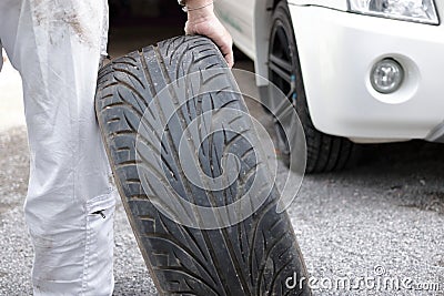 Selective focus on hands of automotive mechanic in uniform holding tire for fixing car at the repair garage background. Stock Photo