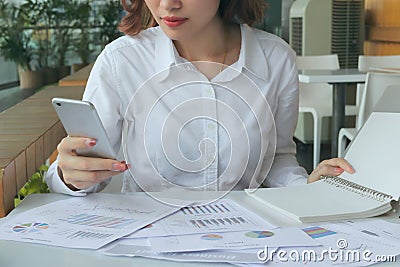 Selective focus on hands of business woman holding mobile smart phone with charts or paperwork on workplace in office Stock Photo