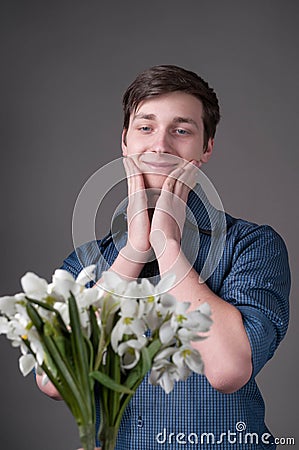 Handsome surprised smiling young man with dark hair in blue shirt with rolled sleeves holding cheeks and looking at bouguet Stock Photo