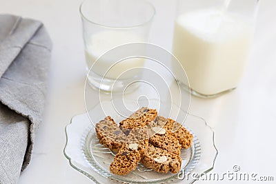 Almond and chocolate biscotti in vintage scalloped glass plate, with grey serviette and bottle and small glass of milk Stock Photo