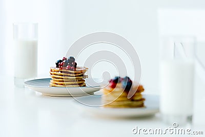 selective focus of homemade pancakes with berries and honey and glasses of milk on tabletop Stock Photo