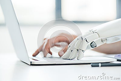 selective focus of human and robot hands typing on laptop Stock Photo