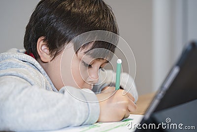 Selective focus kid using green pe colouring, Candid shot child painting on white paper with burrly tablet foreground, Young boy Stock Photo
