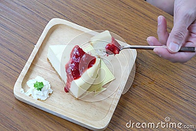 In selective focus a man hand holding a spoon with a piece of chesse cake,wooden plate Stock Photo