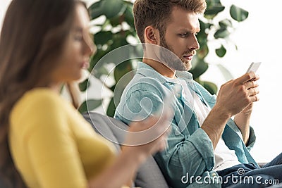 Focus of man using smartphone near girlfriend chatting on couch Stock Photo