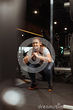 Focus of overweight girl squatting with clenched hands in gym Stock Photo