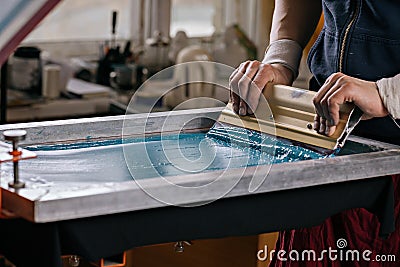 Selective focus photo of male hands with squeegee. serigraphy production. printing images on t-shirts by silkscreen method in a Stock Photo