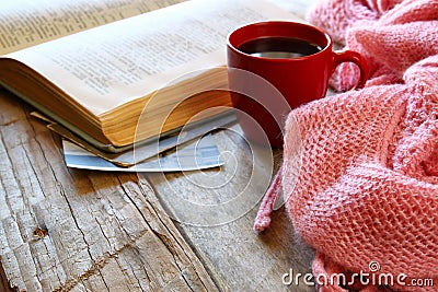 Selective focus photo of pink cozy knitted scarf with to cup of coffee, wool yarn balls and open book on a wooden table Stock Photo