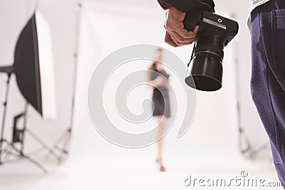 Selective focus of photographer holding camera in a photoshoot with blurry model at the background, behind the scene of model Stock Photo