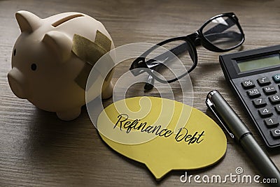 Selective focus of piggy bank, glasses. calculator, pen and yellow speech bubble written with Refinance Debt on wooden background Stock Photo