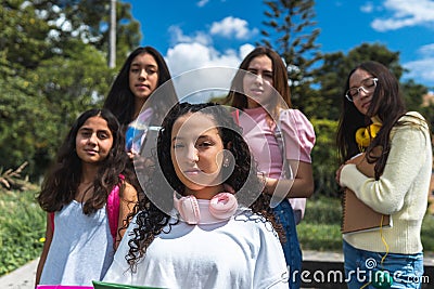 Selective focus portrait of a teenage student with curly hair wearing pink headphones on her neck with four girlfriends out of Stock Photo