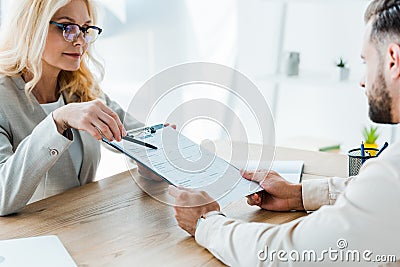Focus of recruiter holding clipboard and pen and sitting near employee Stock Photo