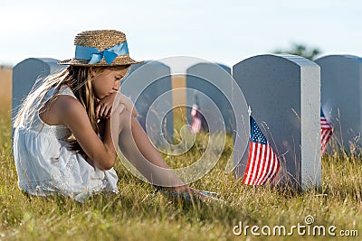 Focus of sad child sitting and looking at headstones with american flags Stock Photo