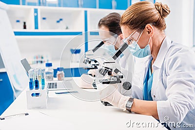 selective focus of scientists in medical masks and goggles looking through microscopes on regents Stock Photo