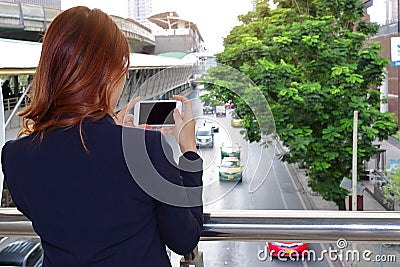 Selective focus and shallow depth of field. Back view of woman taking a photo of traffic car in city with mobile smart phone Stock Photo