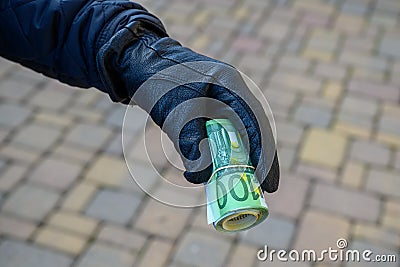 Selective focus shot of a hand wearing a leather glove holding a roll of euro banknotes Stock Photo