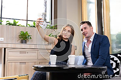 Selective focus at smartphone. Young Caucasian couple dating inside of the coffee shop while women taking selfie photo from mobile Stock Photo