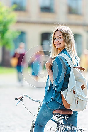 selective focus smiling young student with backpack on bicycle looking at camera Stock Photo