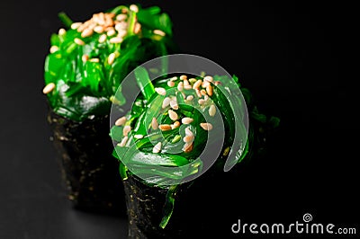 Selective focus on tasty gunkan sushi rolls with chuka seaweed and sesame seeds on black background. Stock Photo