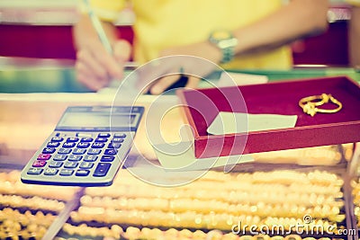 Selective focus to the calculator to calculate the purchase of gold jewelry with blurry staff holding ticket Stock Photo