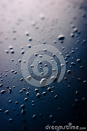 Selective focus on water drops on slippy surface of black synthetic fabric with bright light from background Stock Photo