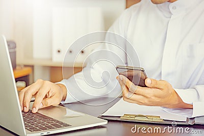 Selective focus of Young business Arab Middle East muslim man using mobile smart phone with laptop in office Editorial Stock Photo