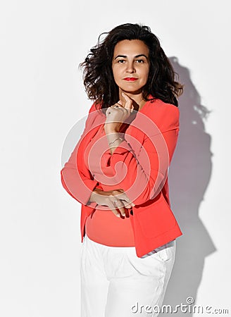 Self-confident business woman in elegant coral shirt, jacket and white pants listens intently holding hand at her chin Stock Photo