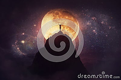 Self overcome concept as a person raising hands up on the top of a mountain over full moon night background. Conquering obstacles Stock Photo