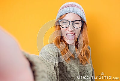 Selfie. Close-up funny mocked woman takes photo of himself with her smartphone while tongue sticking out, isolated on yellow Stock Photo