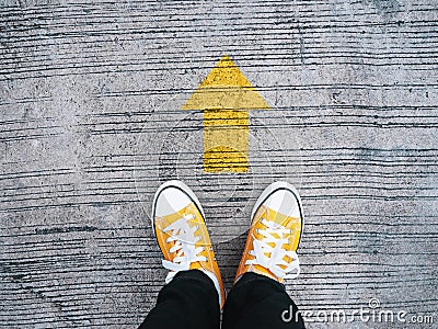 Selfie feet wearing yellow sneakers in front of arrow on concrete road Stock Photo