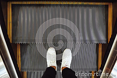 Selfie of man feet in white sneaker shoes on escalator steps in the shopping mall top view in vintage style Stock Photo