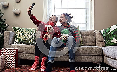 Selfie time. a cheerful young couple holding their pet dogs while taking a selfie and being seated on a sofa during Stock Photo