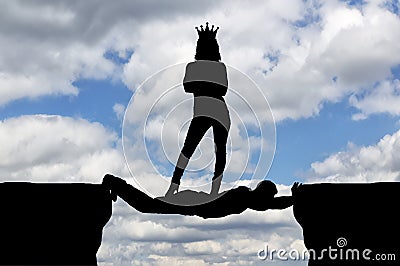 Selfish woman with a crown standing on a man in the form of a bridge over an abyss Stock Photo