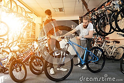 A seller at a bicycle store helps a young buyer choose a new mountain bike. Stock Photo